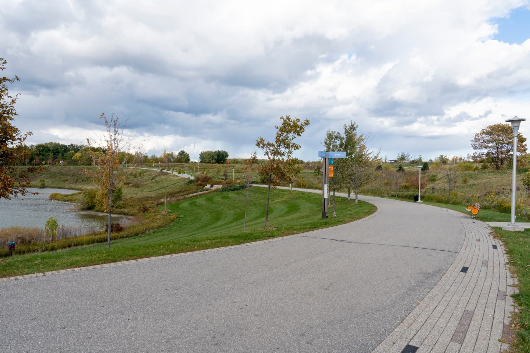 A lakeside walking path through Downsview Park with autumn trees and benches